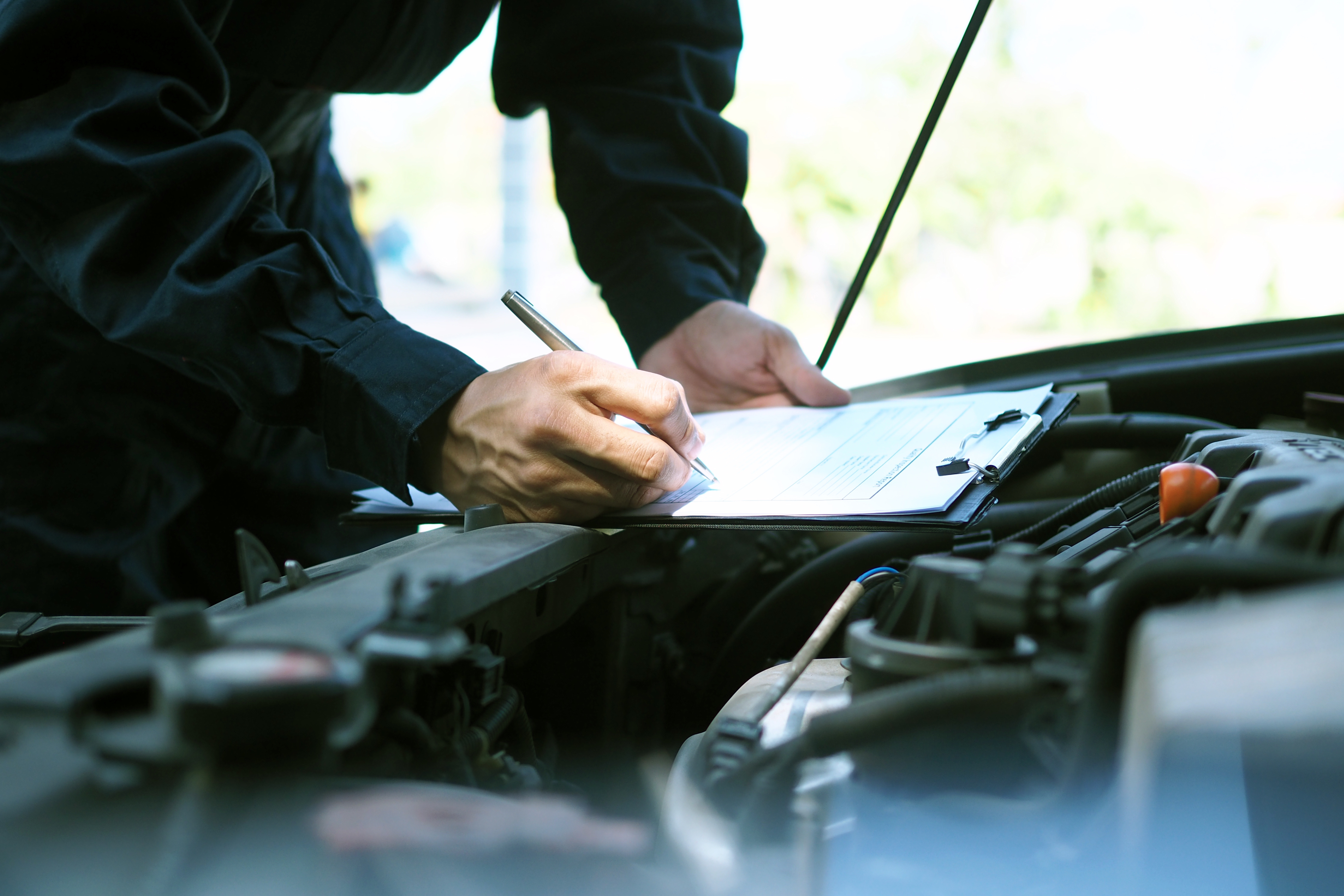 Engineer inspecting engine and taking notes on vehicle checklist
